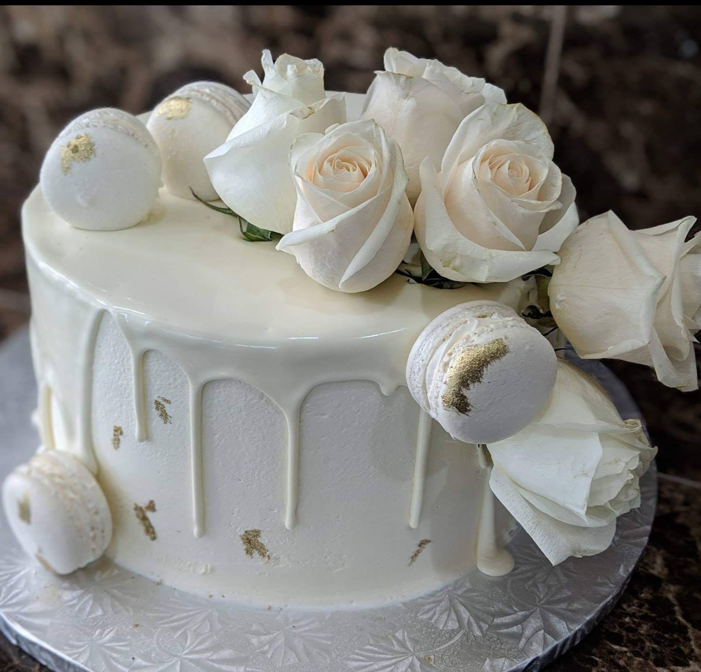 Elegant white drip cake adorned with fresh white roses, gold-leafed macarons, and delicate gold accents