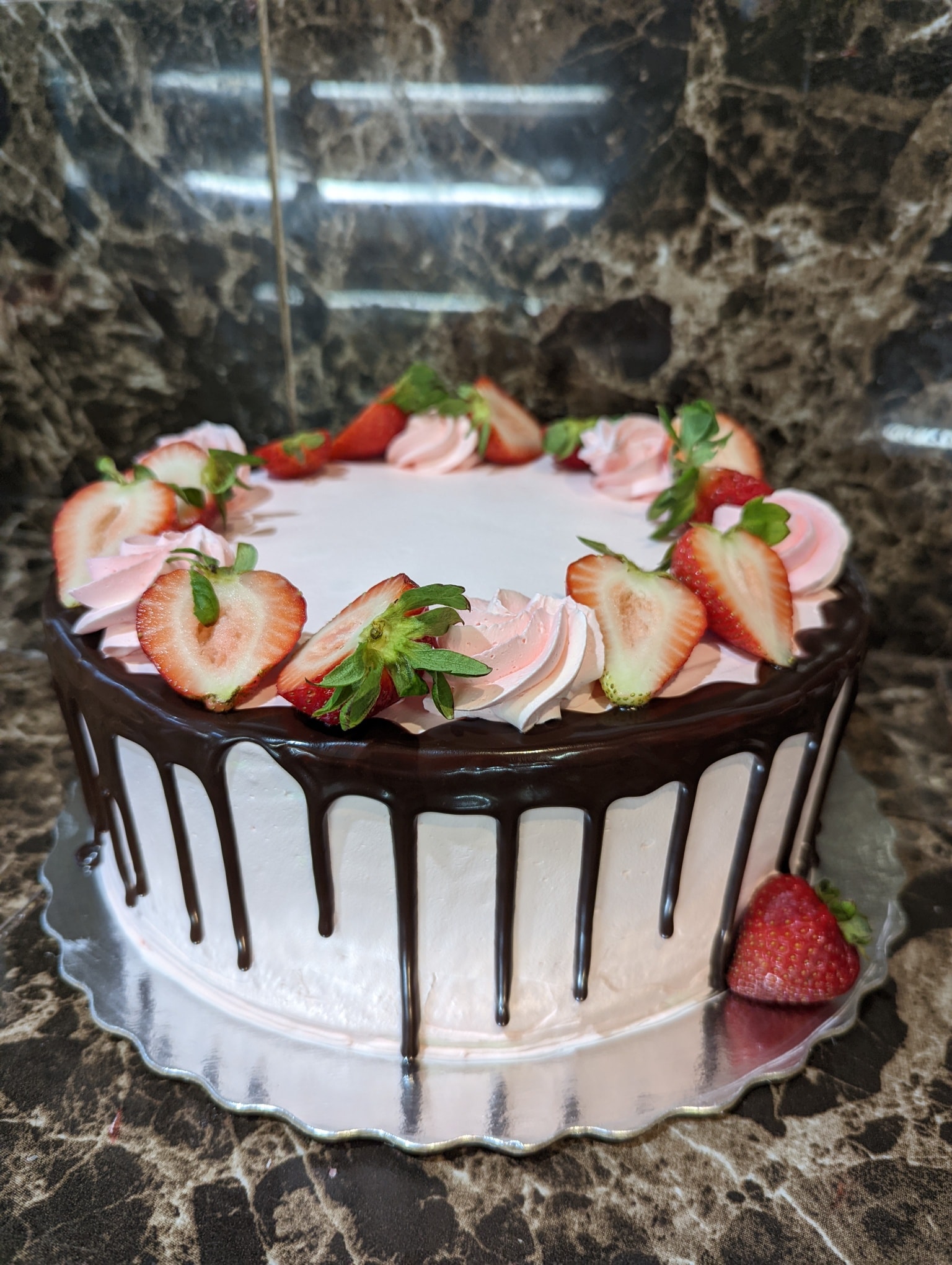 Chocolate drip cake decorated with fresh strawberries and pink cream rosettes