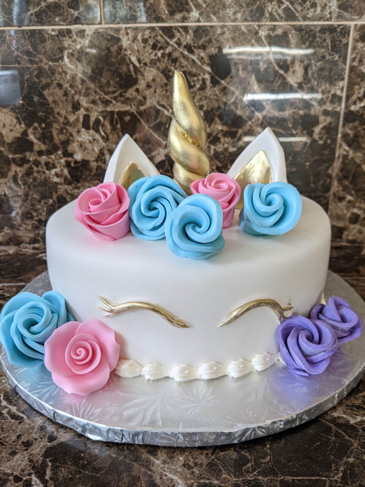Whimsical unicorn birthday cake with colorful buttercream roses and golden horn