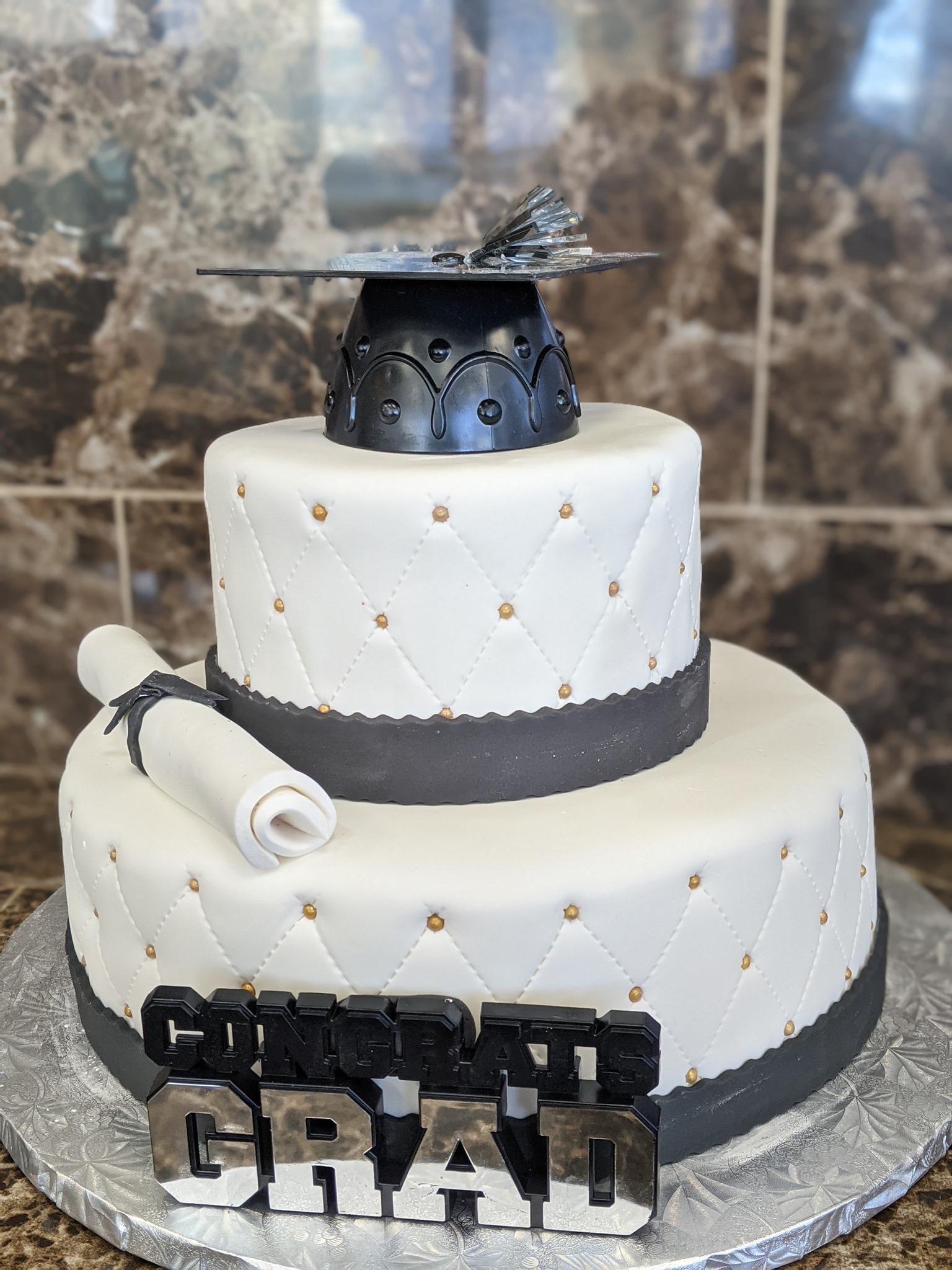Two-tier quilted graduation cake with gold accents, graduation cap, and diploma topper