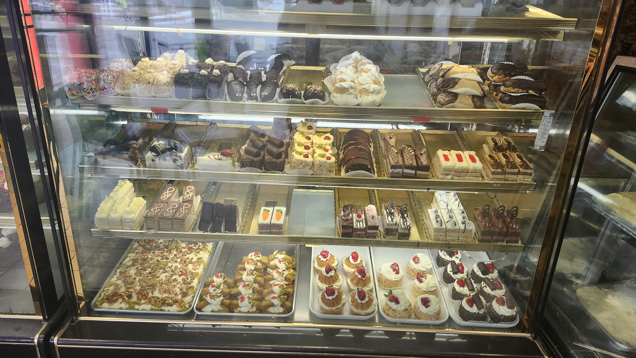 Three shelves of elegant European petit fours, eclairs, cream puffs, and miniature pastries