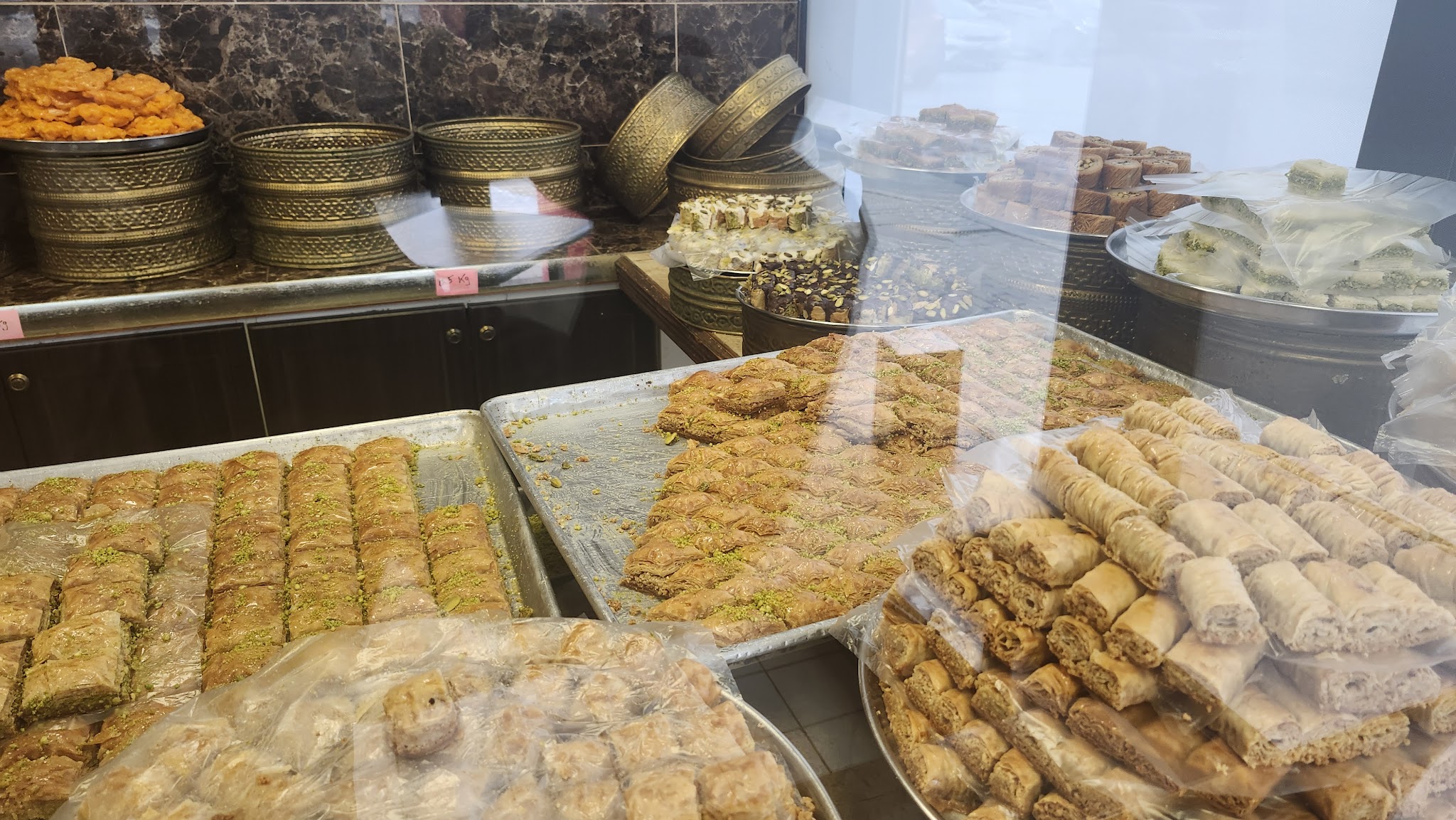 Display case filled with rows of golden baklava, traditional pastries in ornate bowls, and assorted Middle Eastern sweets at La Brioche
