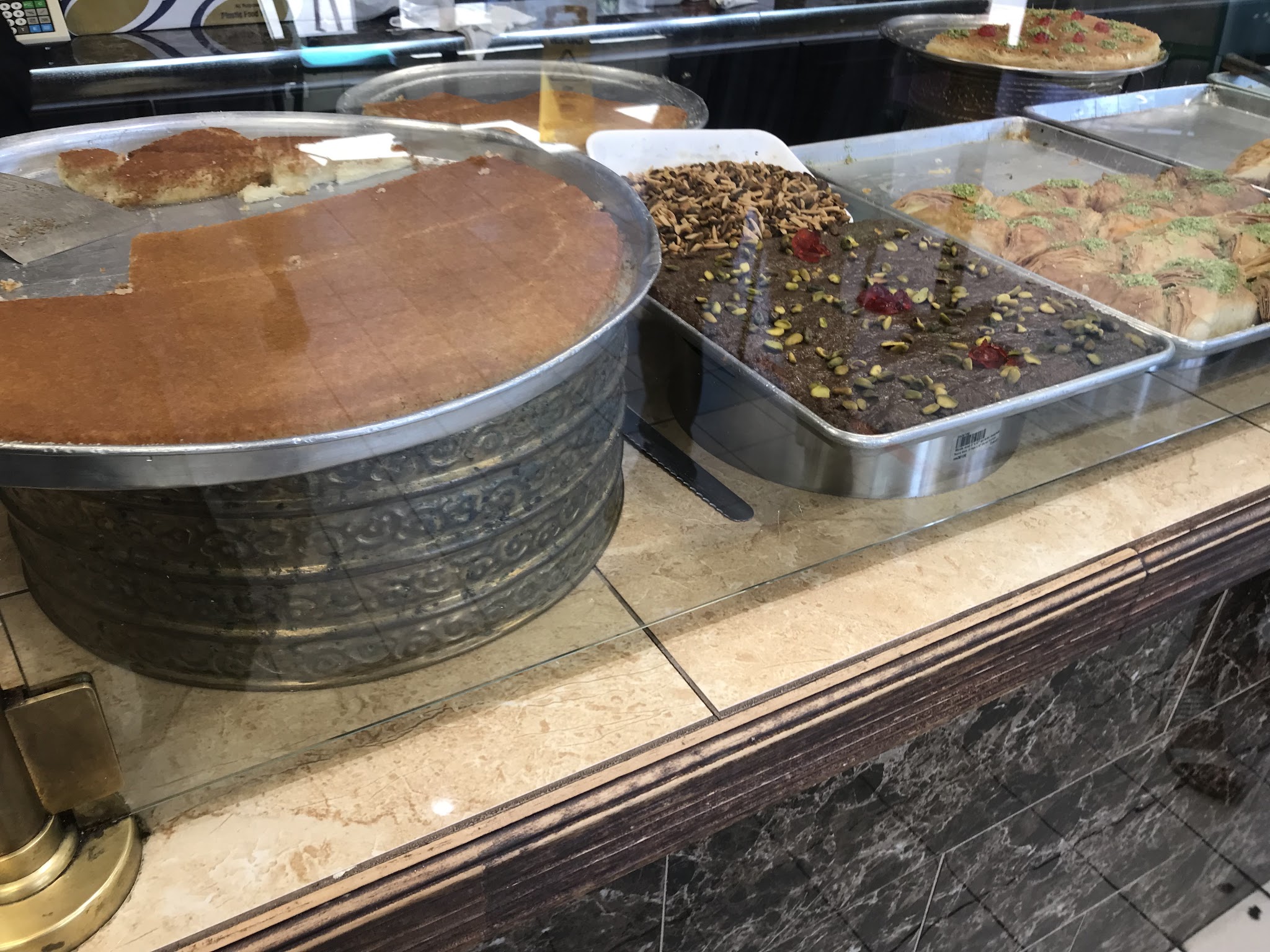 Kunafa in brass bowl with chocolate pastries at the bakery counter