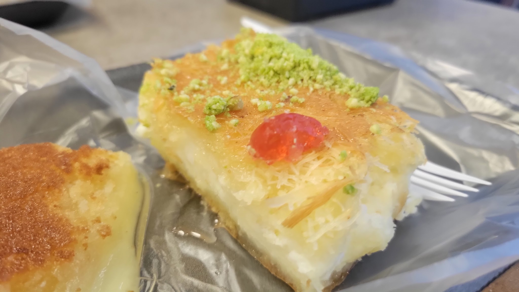 A generous slice of kunafa with golden crispy top, creamy cheese filling, crushed pistachio, and a cherry