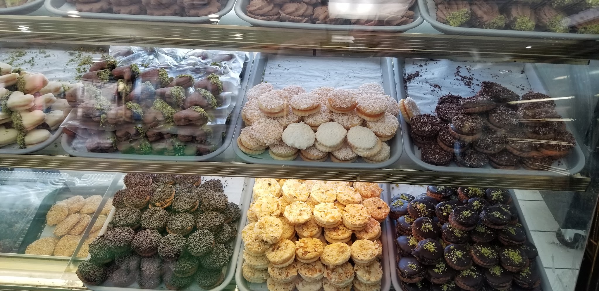 Colorful display of petit fours and cookies in neat rows — sesame, pistachio, chocolate, and almond varieties