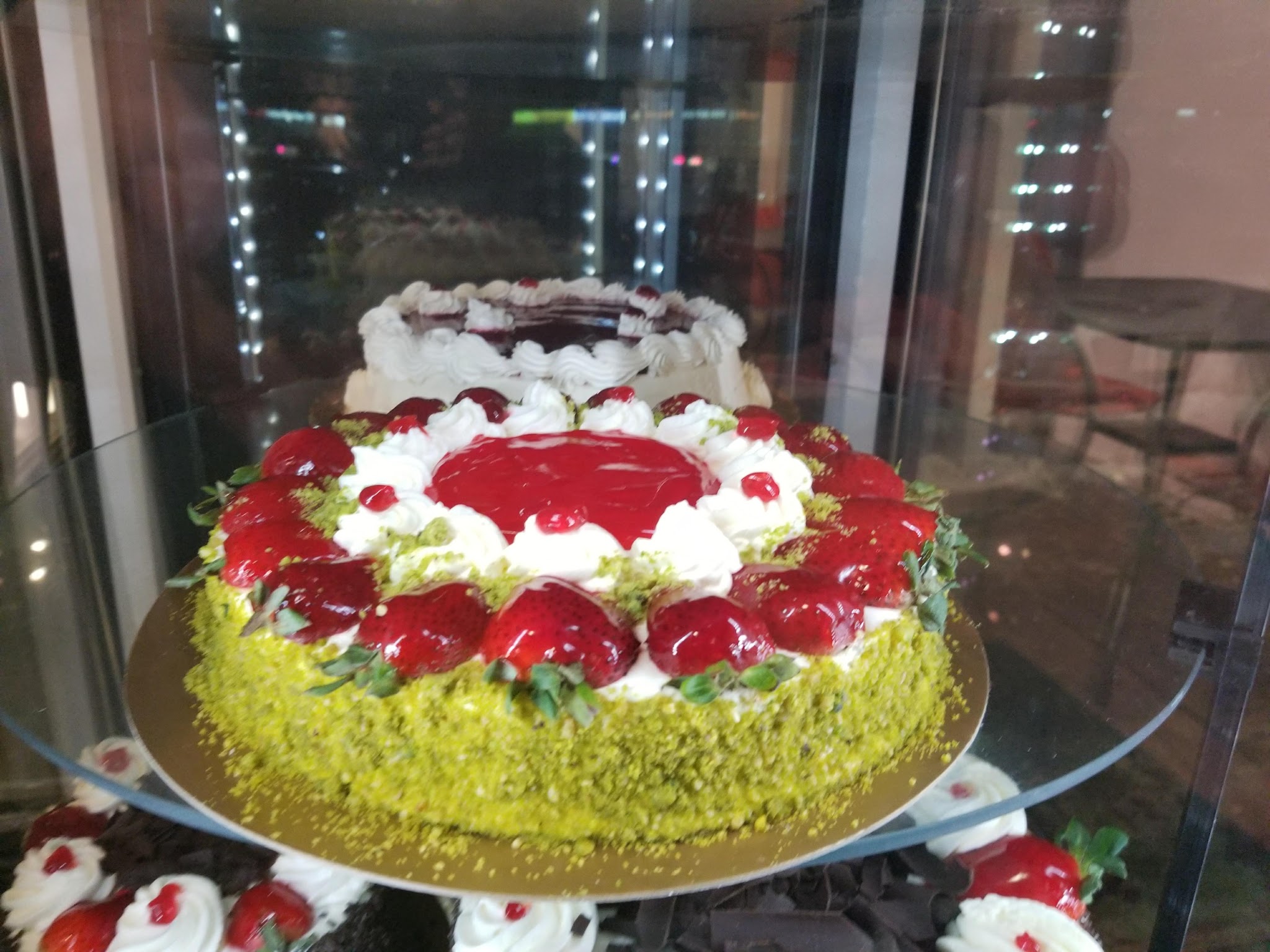 Stunning strawberry fruit torte with glazed strawberries, cream, and pistachio crust in the display case