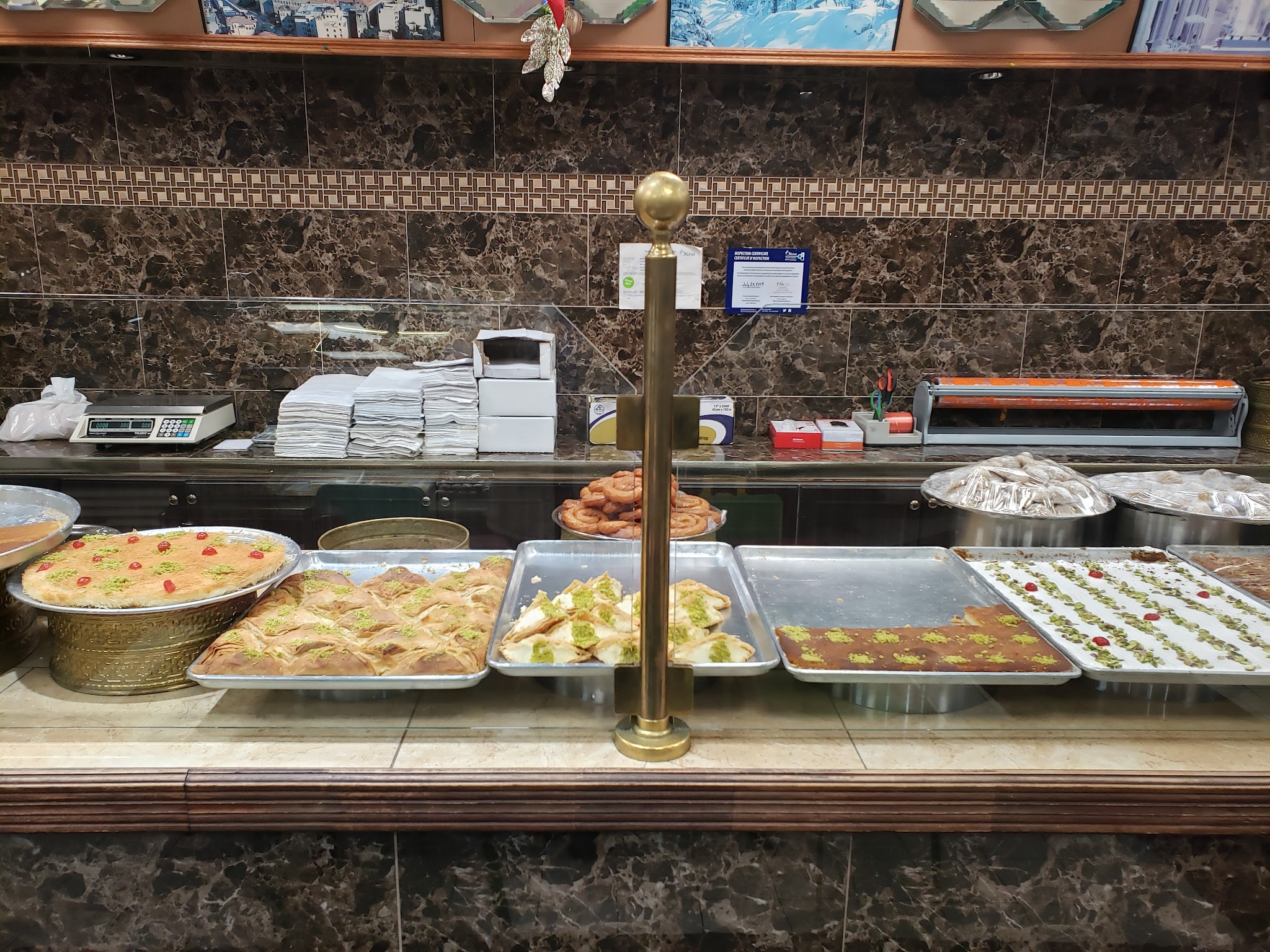 The bakery counter with traditional brass posts, trays of Middle Eastern pastries, and photos of Lebanon on display